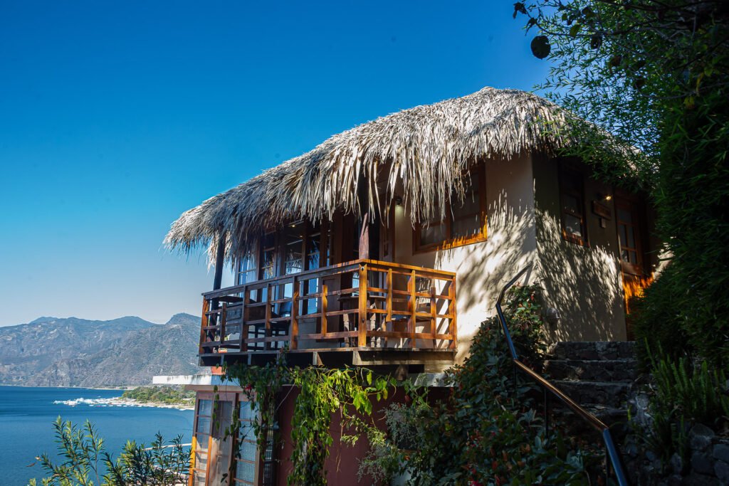 Villa Soluna with thatched roof overlooking Lake Atitlan, Guatemala. Lush greenery and mountains in the background.