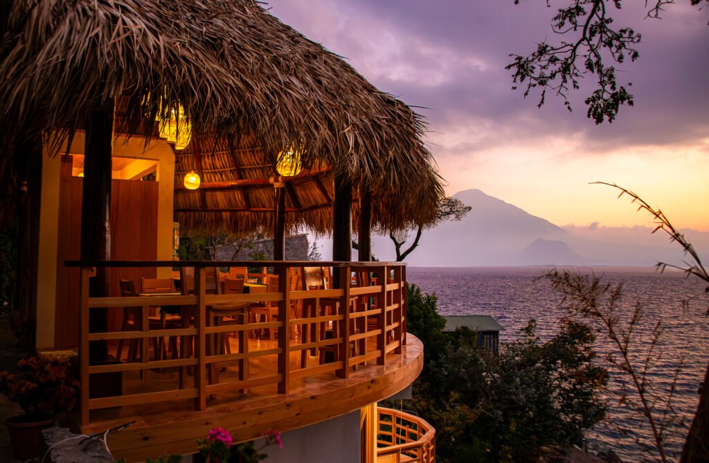 B'alam Ya Cafe view: Thatched roof palapa overlooking Lake Atitlán at sunset with a volcano backdrop.