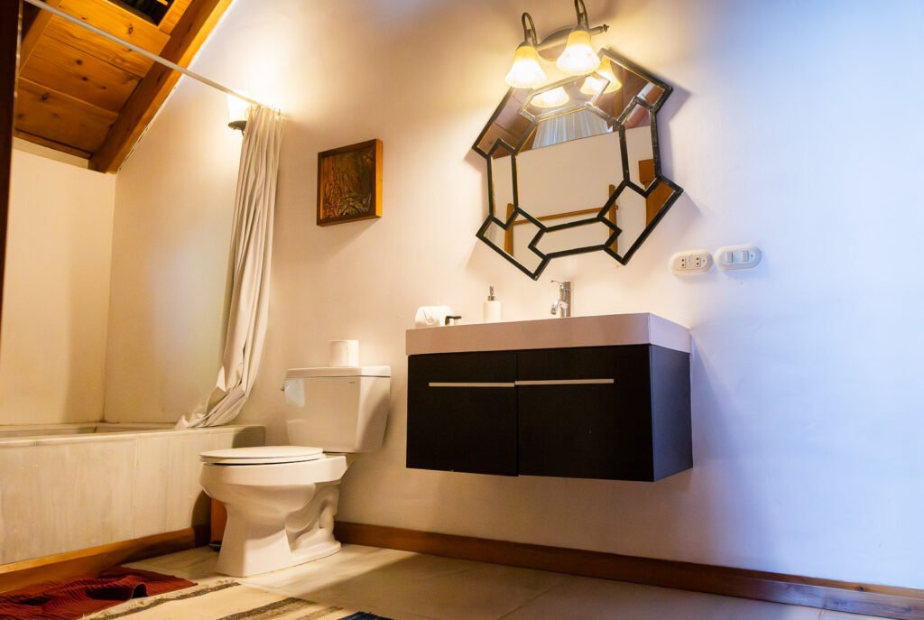 Villa Bambu bathroom with black vanity, unique mirror, toilet, and bathtub with shower curtain.