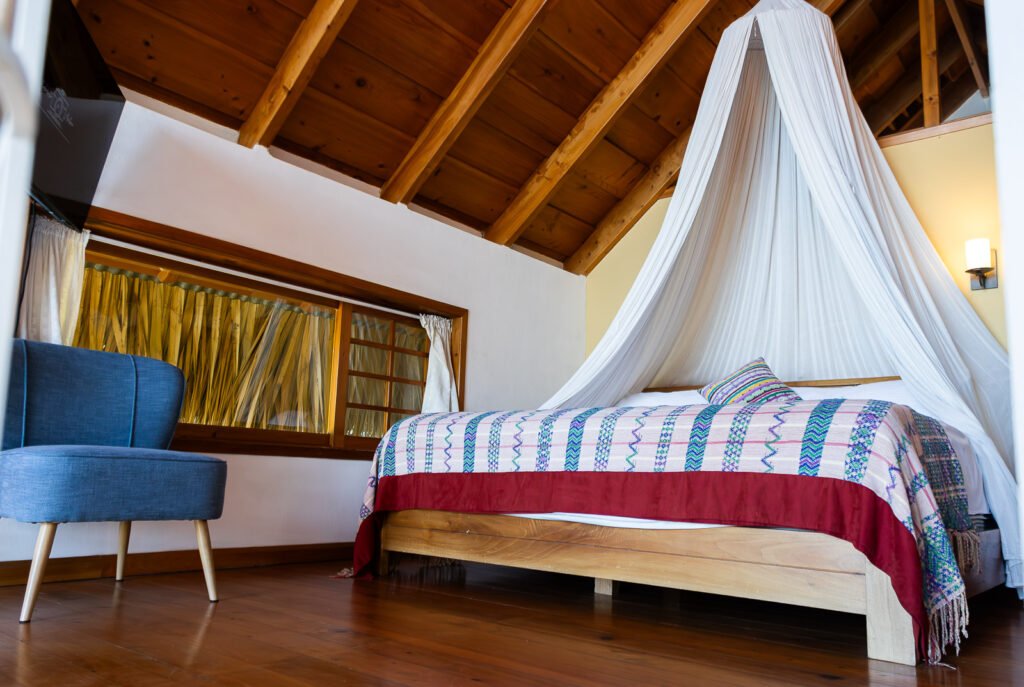 Villa Bambu bedroom with wood ceiling, four-poster bed, blue chair, and hardwood floors.