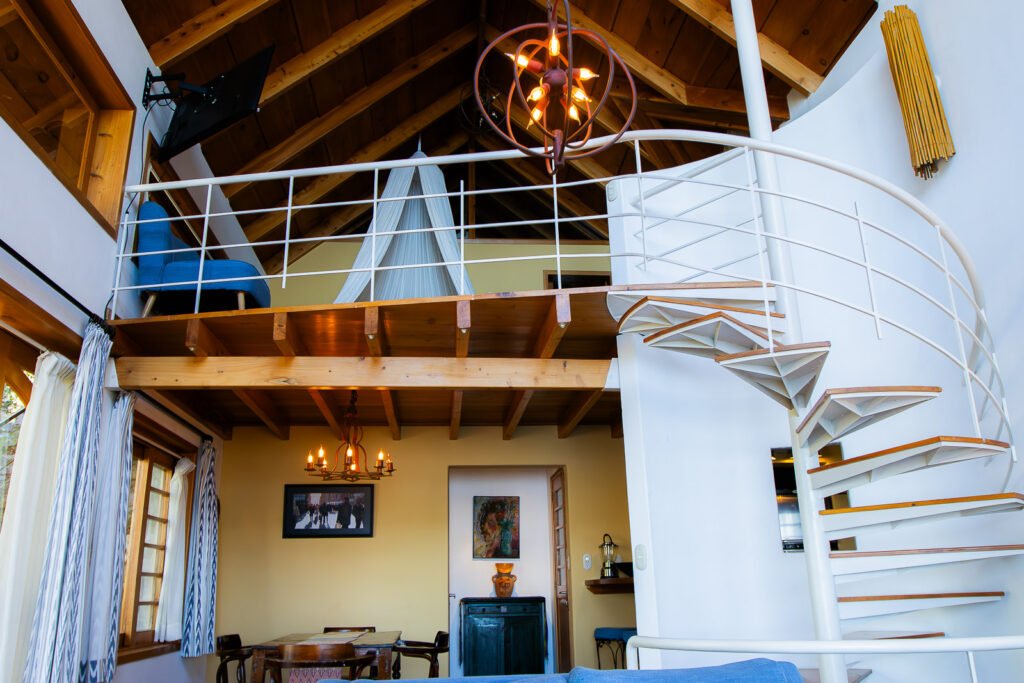 Villa Bambu interior: Spiral staircase, loft with blue chair, and dining area under wooden beams.