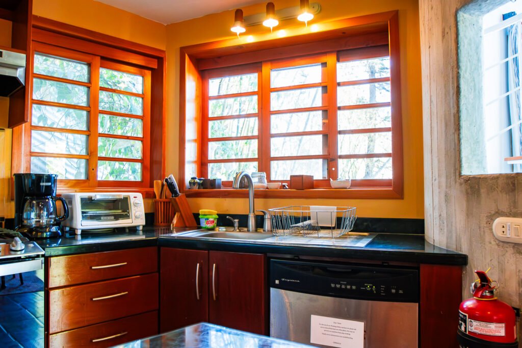 Villa Bambu kitchen with wood windows, black countertops, stainless steel dishwasher, and warm orange walls.
