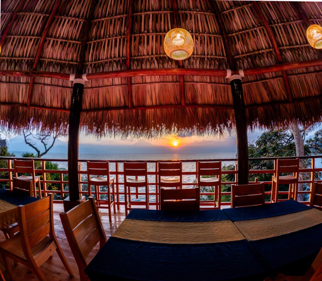 Sunset view from B'alam Ya Cafe, showcasing the lake and volcano from a thatched-roof structure.
