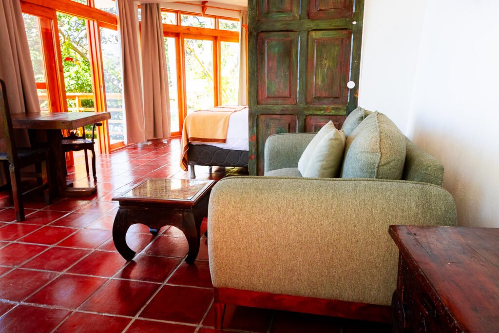 Villa Gio interior with terracotta tile floor, green sofa, and rustic wooden furniture near a bright window.