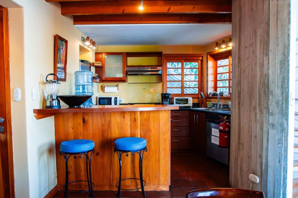 Villa Bambu kitchen with wood bar, blue stools, and window.