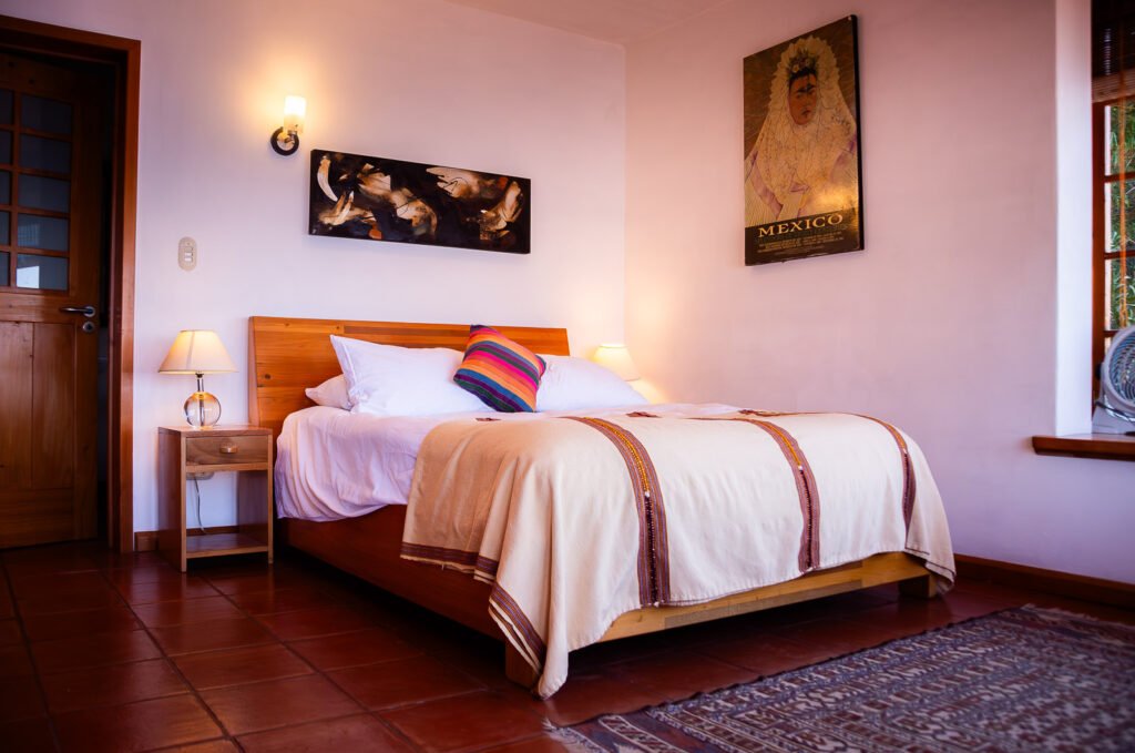 Villa Mirador bedroom with a wooden bed, colorful pillow, and Mexican art.