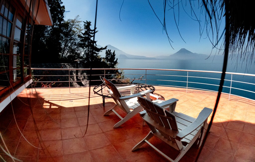 Villa Mirador balcony view with chairs overlooking a lake and distant mountains.