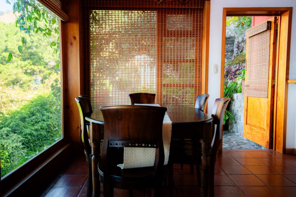 Dining area at Villa Mirador with wooden table, chairs, and a view of lush greenery.