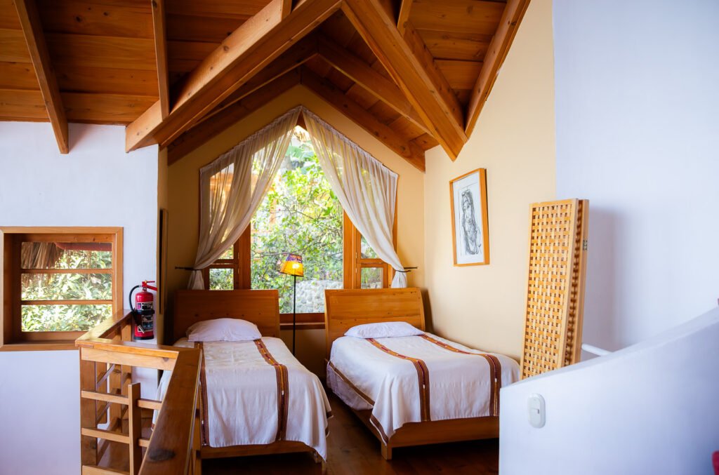 Villa Mirador's cozy loft bedroom with twin beds, wooden beams, and a bright window.