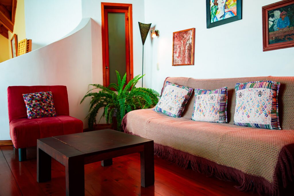 Villa Mirador living room with red chair, couch, and dark wood table on a red wood floor.