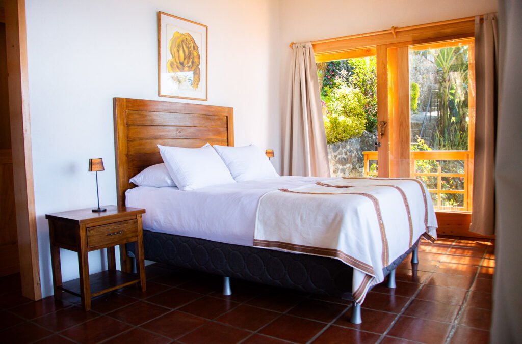 Villa Shakti bedroom with wooden headboard, white linens, and garden view through open doors.