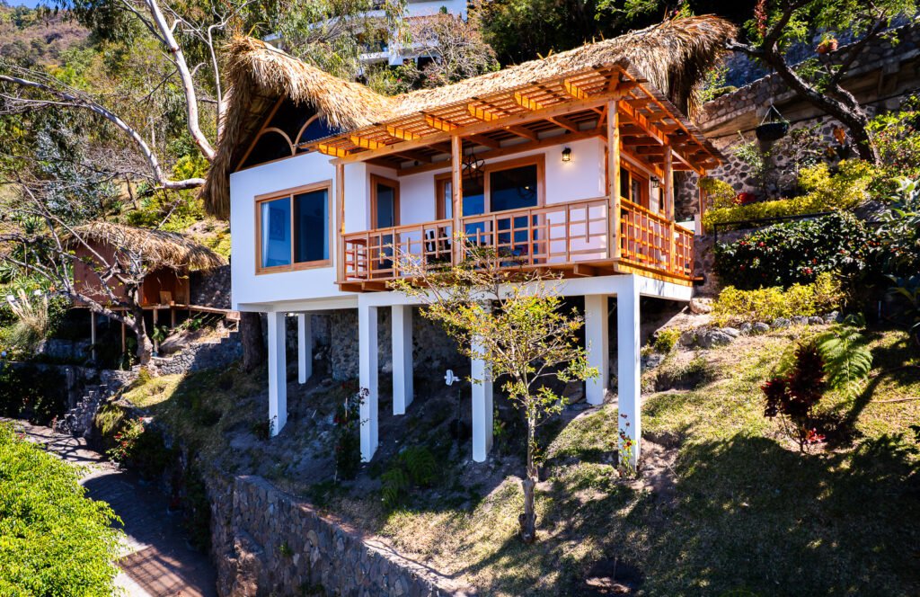 Villa Shakti: Elevated bungalow with thatched roof and wooden balcony on a lush hillside.