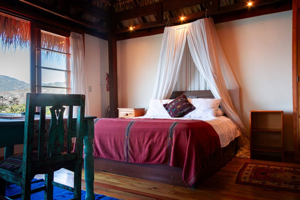 Villa Soluna bedroom with four-poster bed, red blanket, and view of the mountains.
